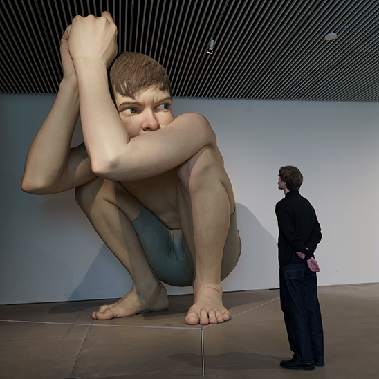 A person looking at the 4.5-meter tall hyper-realistic sculpture of 'Boy' by Ron Mueck